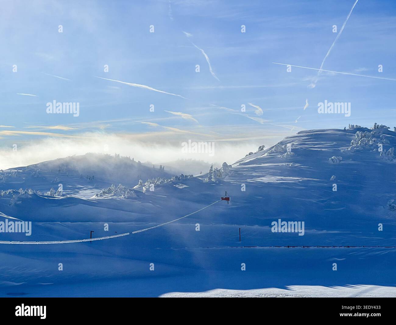 Forêt enneigée et pistes de ski sur la montagne Jahorina sous les nuages hivernaux spectaculaires et le ciel bleu. - Image de stock capturée avec un smartphone