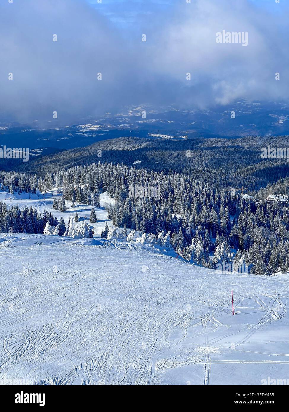Forêt enneigée et pistes de ski sur la montagne Jahorina sous les nuages hivernaux spectaculaires et le ciel bleu. - Image de stock capturée avec un smartphone