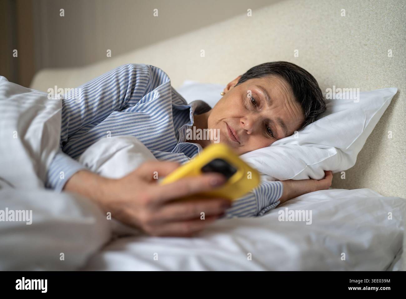 Femme âgée paresseuse avec dépendance au téléphone couchée dans le lit le matin procrastinant temps défile en ligne. Banque D'Images