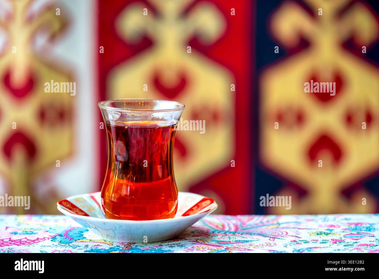Verre armudu en forme de poire avec du thé noir sur une soucoupe décorée, avec un tapis traditionnel azerbaïdjanais en arrière-plan, Azerbaïdjan. Banque D'Images