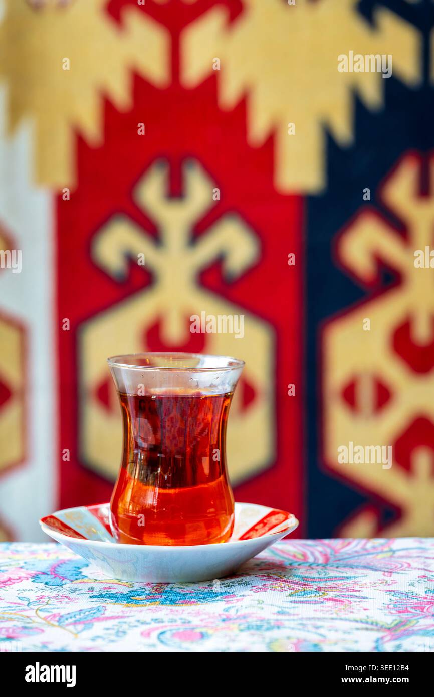 Verre armudu en forme de poire avec du thé noir sur une soucoupe décorée, avec un tapis traditionnel azerbaïdjanais en arrière-plan, Azerbaïdjan. Banque D'Images