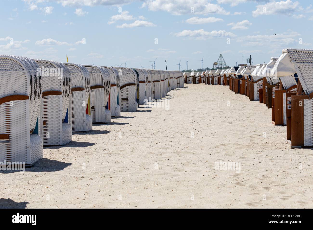 Vue sur les rangées de chaises de plage traditionnelles à capuche en osier blanc sur le sablonneux Strand Schillig sous un ciel lumineux avec des éoliennes dans la distance Wanger Banque D'Images