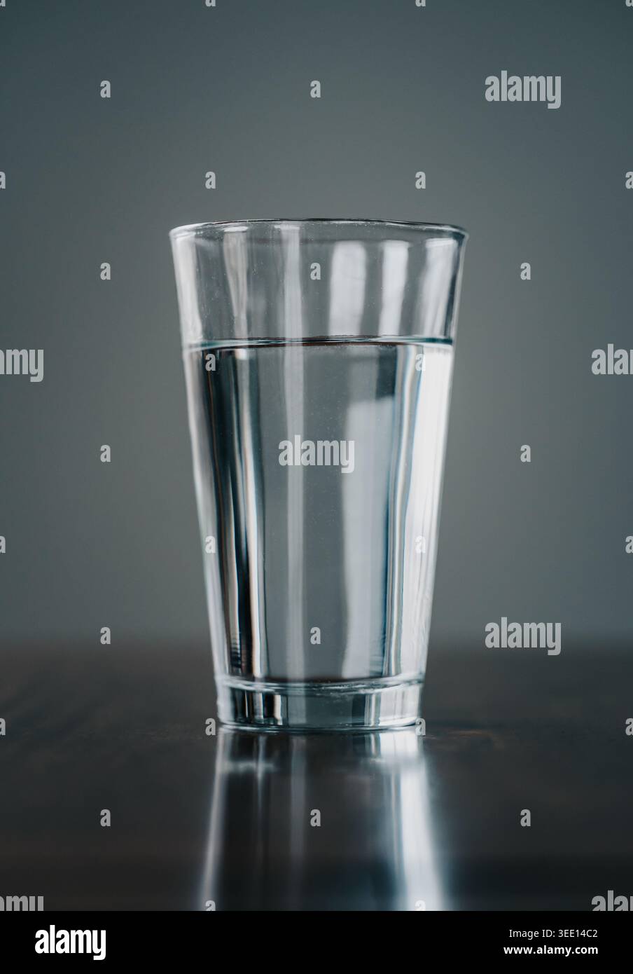Gros plan de grand verre d'eau sur la table en bois avec fond gris. Banque D'Images