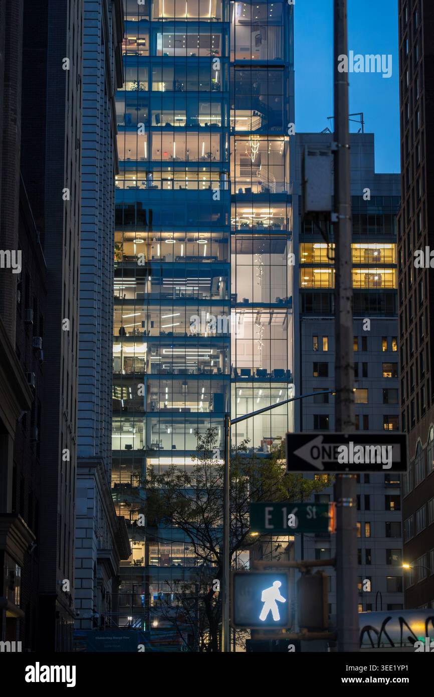 Vue sur un gratte-ciel moderne en verre avec des intérieurs de bureau illuminés au crépuscule, avec un panneau East 16th Street et un signal piétonnier Kings County, ne Banque D'Images