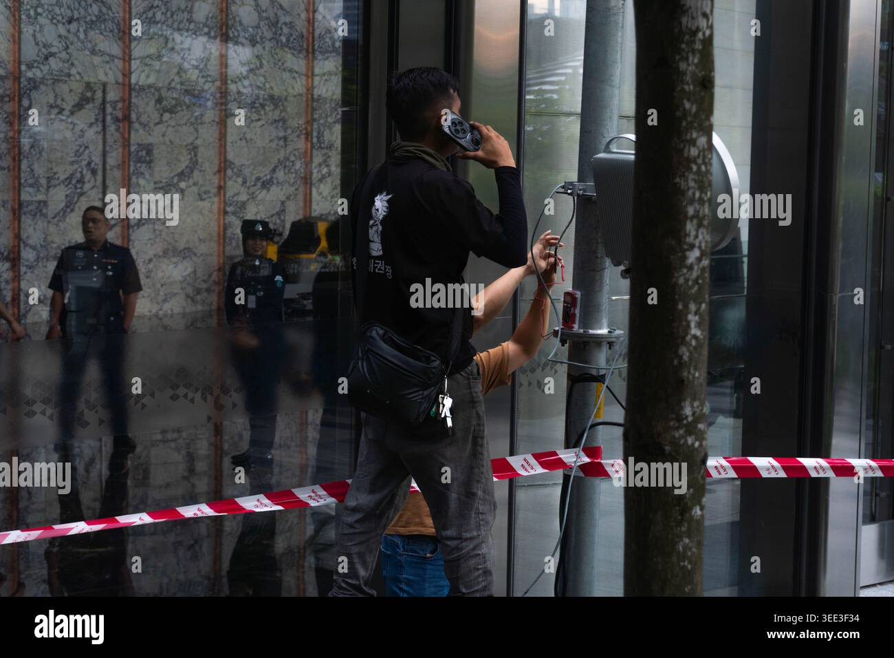 Kuala Lumpur, Malaisie - 25 avril 2026 : deux ouvriers installent une lumière dont l'un porte une chemise noire et parle au téléphone Banque D'Images