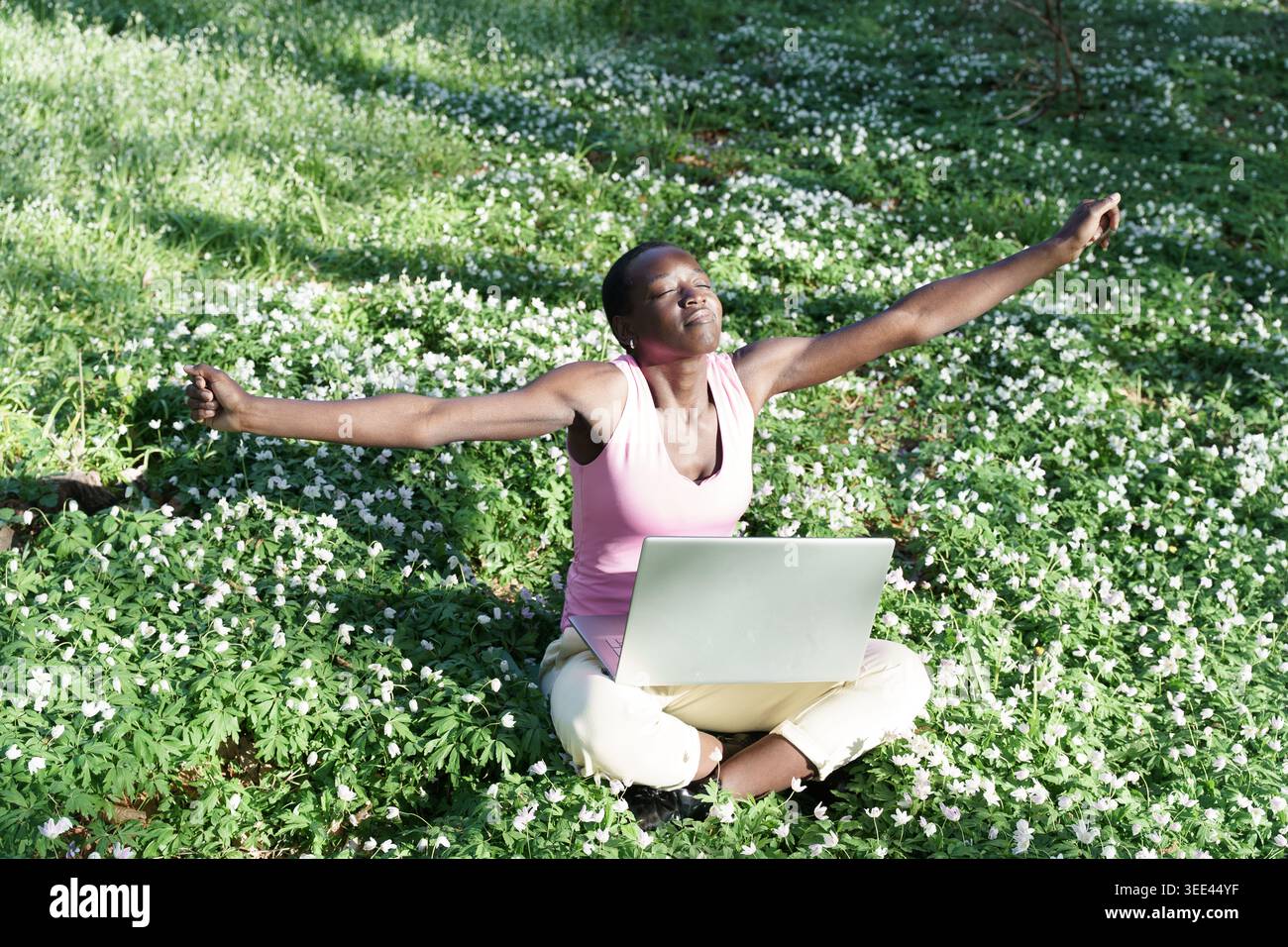 Femme heureuse avec un ordinateur portable étirant les bras dans le travail à distance de liberté de parc forestier de source de fleurs Banque D'Images