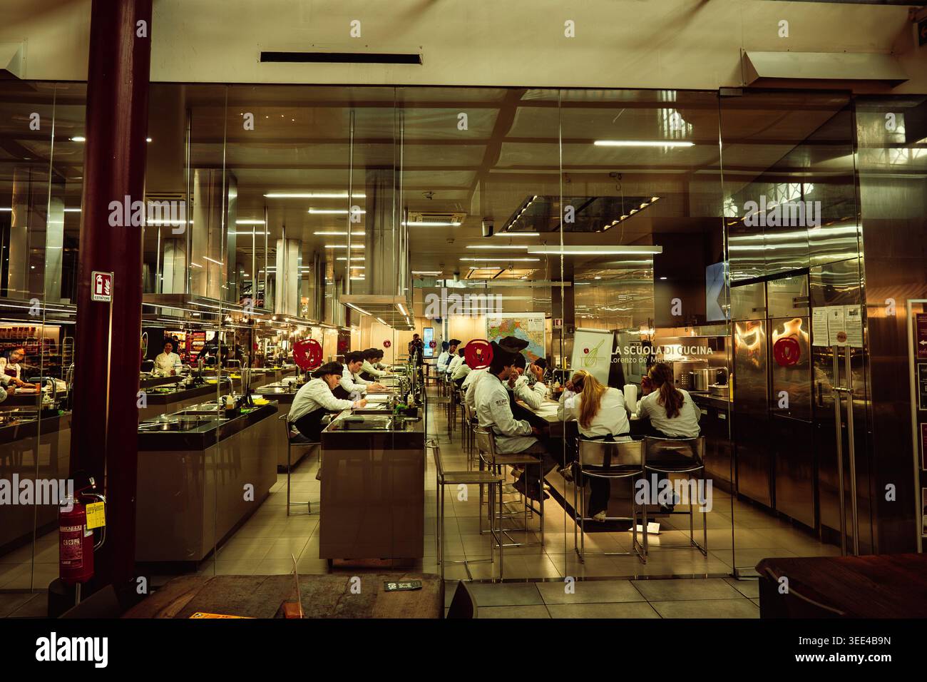 Les étudiants en cuisine en blanc de chef sont vus à travers une cloison en verre, activement engagés dans un cours de cuisine à la Scuola di Cucina à Florence, en Italie. Th Banque D'Images