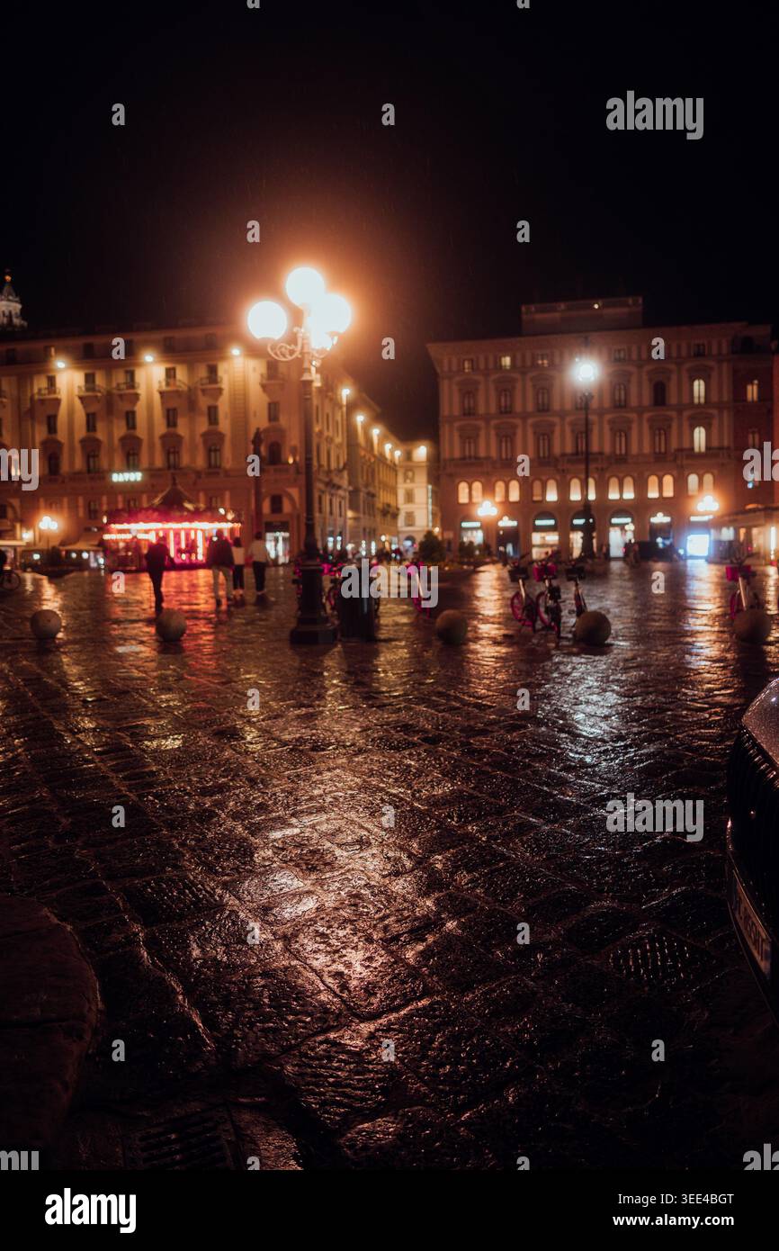 Une scène de rue en soirée à Florence, en Italie, mettant en vedette des pavés humides reflétant la lueur chaude des lampadaires et de la fenêtre éclairée du bâtiment Banque D'Images