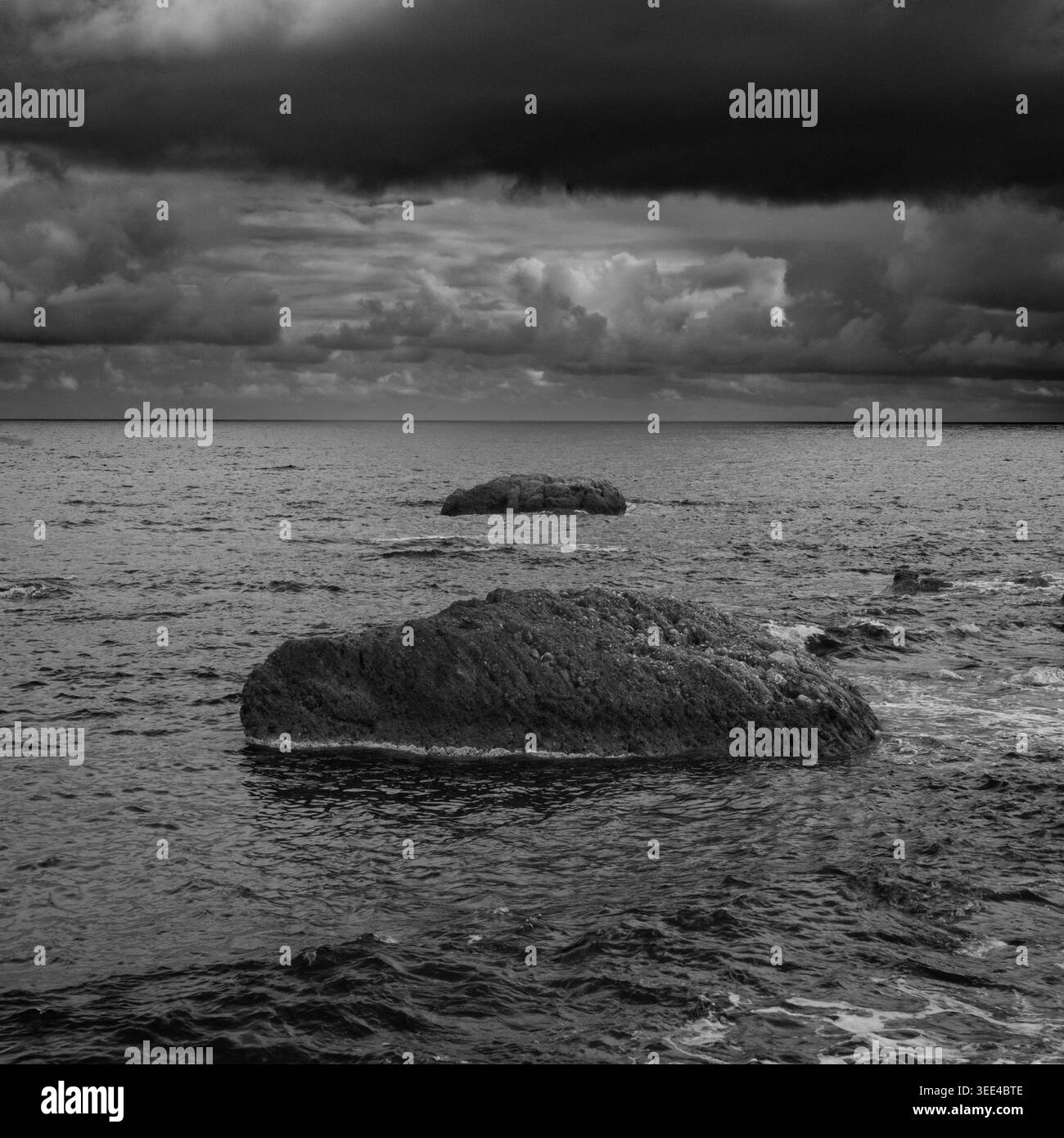 Une photographie en niveaux de gris capturant la beauté sauvage de la mer Ionienne à Giardini Naxos, en Sicile. Deux rochers proéminents émergent des vagues ondulantes und Banque D'Images