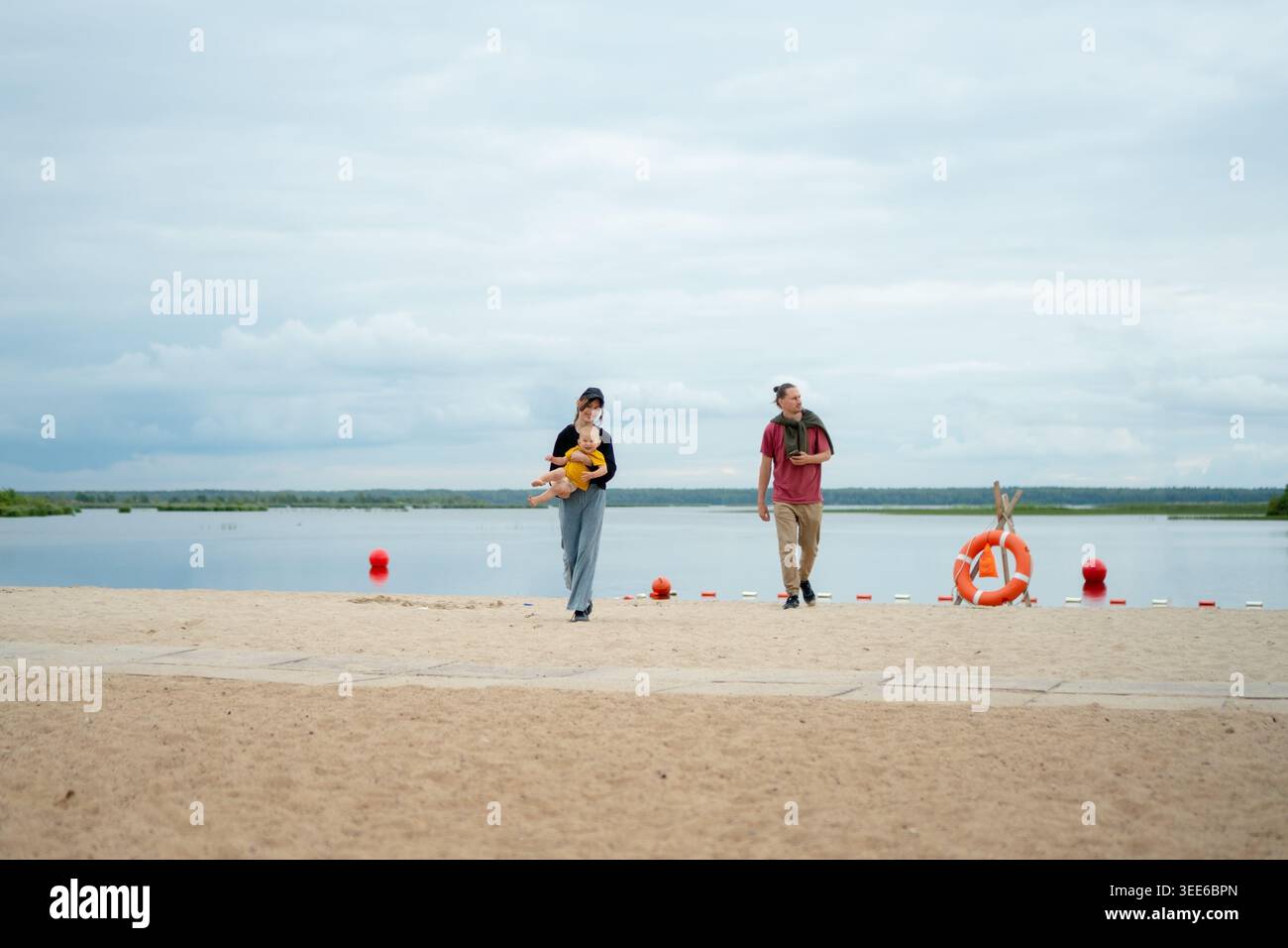 Un homme et une femme se promènent paisiblement le long d'une plage sereine au bord du lac. Le mari et la femme profitent d'une promenade romantique calme ensemble à l'extérieur. Les partenaires partagent un moment de tranquillité sur le front de mer sablonneux Banque D'Images