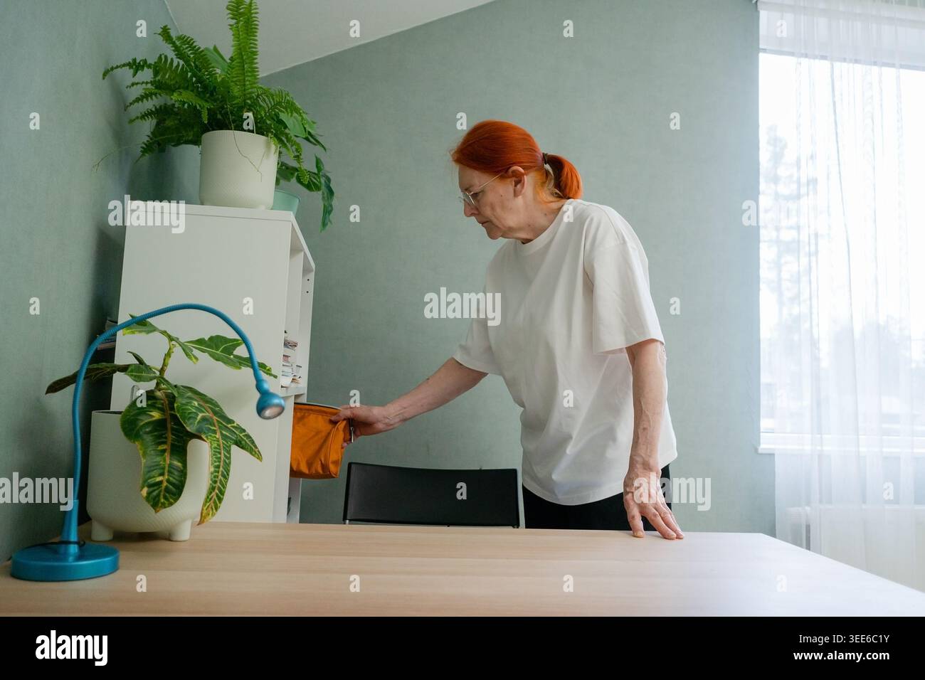 Une femme âgée est en train de ranger, d'organiser soigneusement divers articles et de mettre les choses à leur place dans sa maison. Cette activité reflète son désir d'ordre, de propreté Banque D'Images