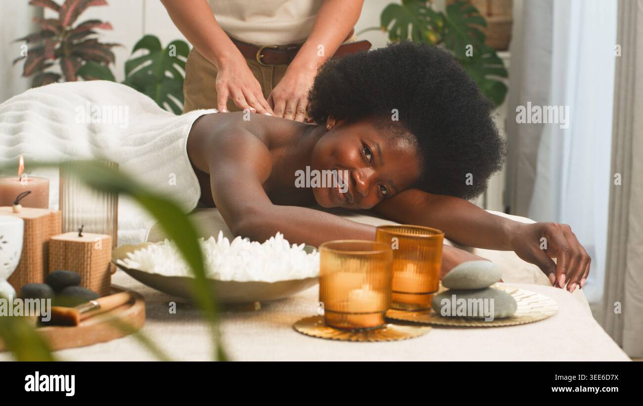 Femme souriante recevant un massage du dos au spa relaxant avec des bougies et des pierres chaudes Banque D'Images