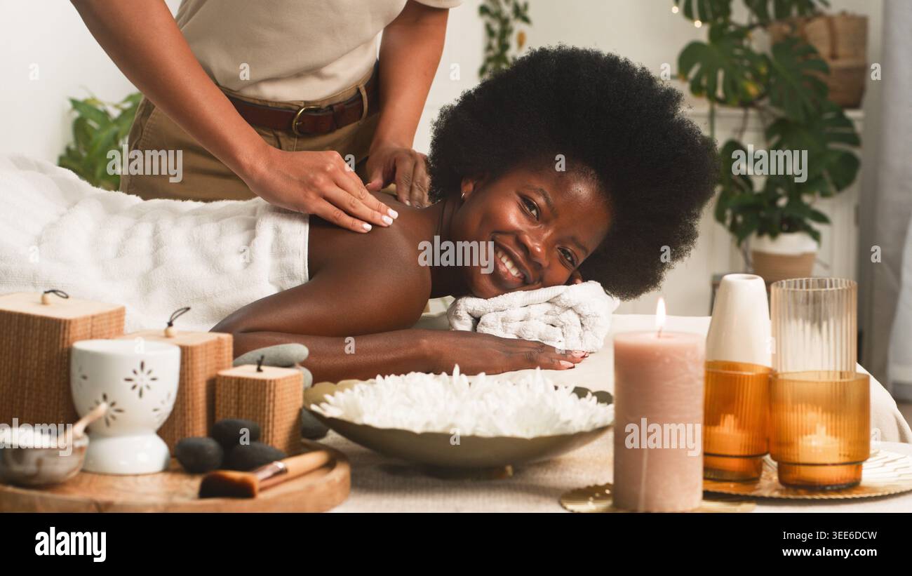 Femme souriante recevant un massage relaxant du dos au Spa avec bougies et aromathérapie Banque D'Images