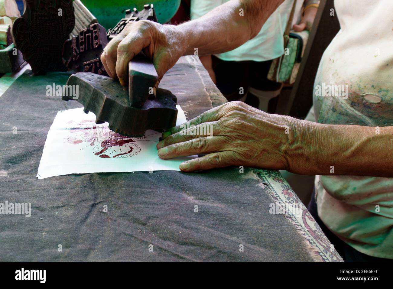 Gros plan des mains artisanales indiennes à l'aide d'un bloc de batik en bois sculpté pour imprimer un motif traditionnel sur tissu Banque D'Images