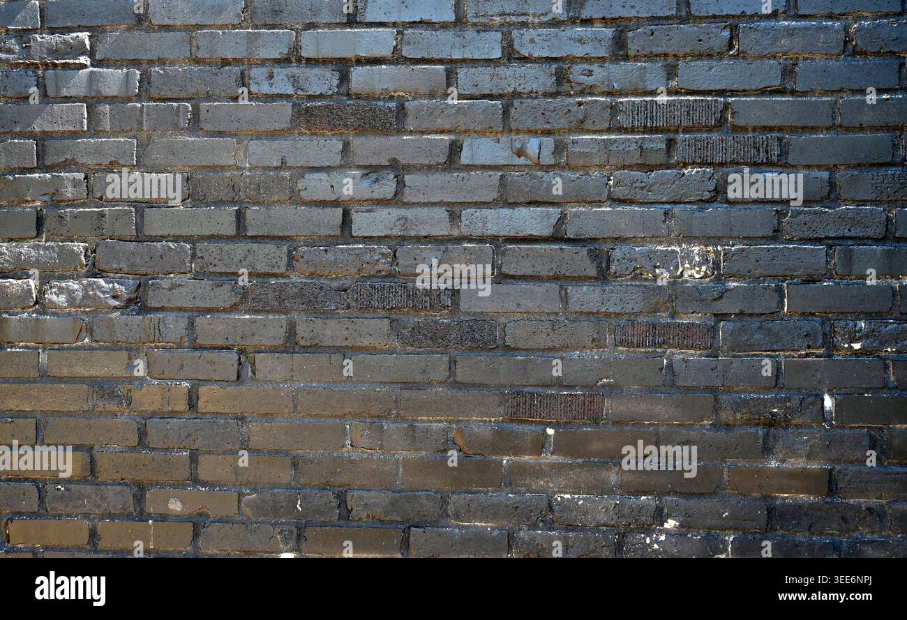 Mur de briques noires peintes avec des briques lisses et rugueuses qui sont fissurées, inégales et ébréchées Banque D'Images