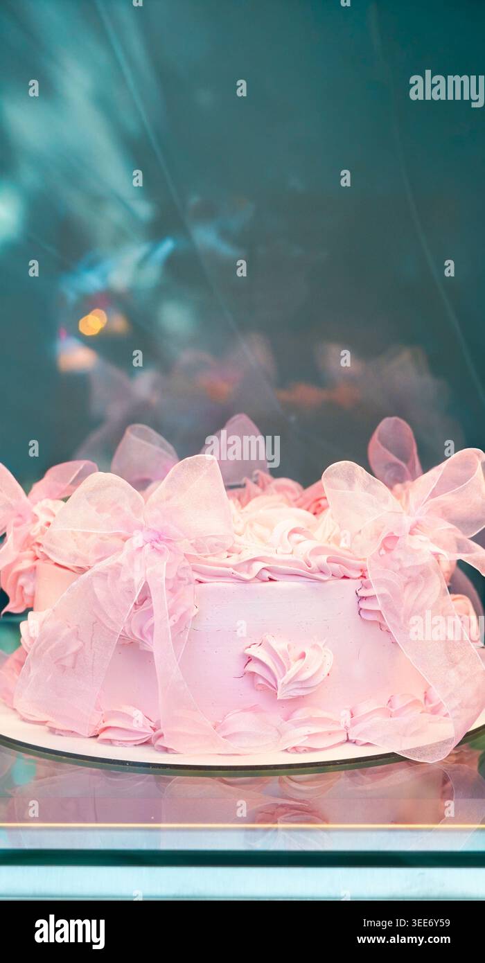 Élégant gâteau dépoli rose décoré avec des noeuds en tissu transparent dans une vitrine Banque D'Images