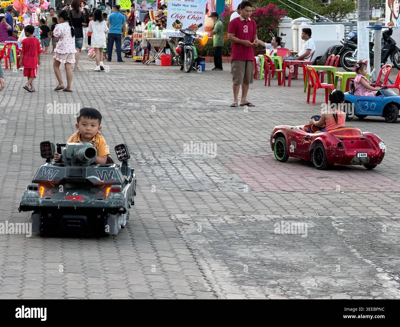 Les parents se joignent au plaisir en contrôlant leurs mini voitures childÕs radiocommandées dans le parc 30 Thang 4 sur la promenade principale de Chau Doc cityÕs, face au confl - Image de stock capturée avec un smartphone