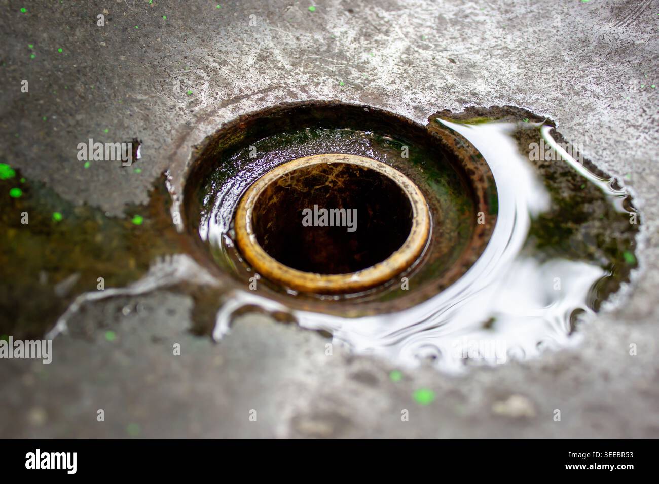 Gros plan d'un trou de drainage d'évier de ciment avec flaque d'eau claire et réflexion de lumière sur une surface rugueuse Banque D'Images
