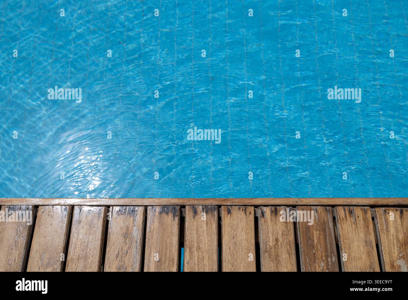 Terrasse en bois à côté de l'eau turquoise lumineuse de la piscine avec des reflets chatoyants et des textures de surface ondulantes créant un calme de loisirs estivaux Banque D'Images