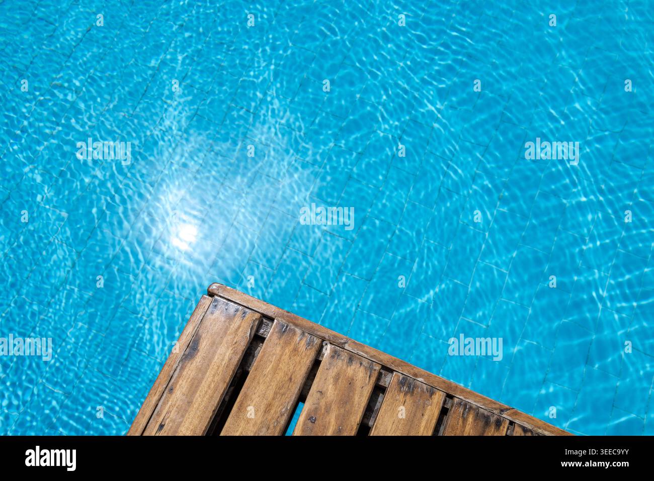 Terrasse en bois à côté de l'eau turquoise lumineuse de la piscine avec des reflets chatoyants et des textures de surface ondulantes créant un calme de loisirs estivaux Banque D'Images