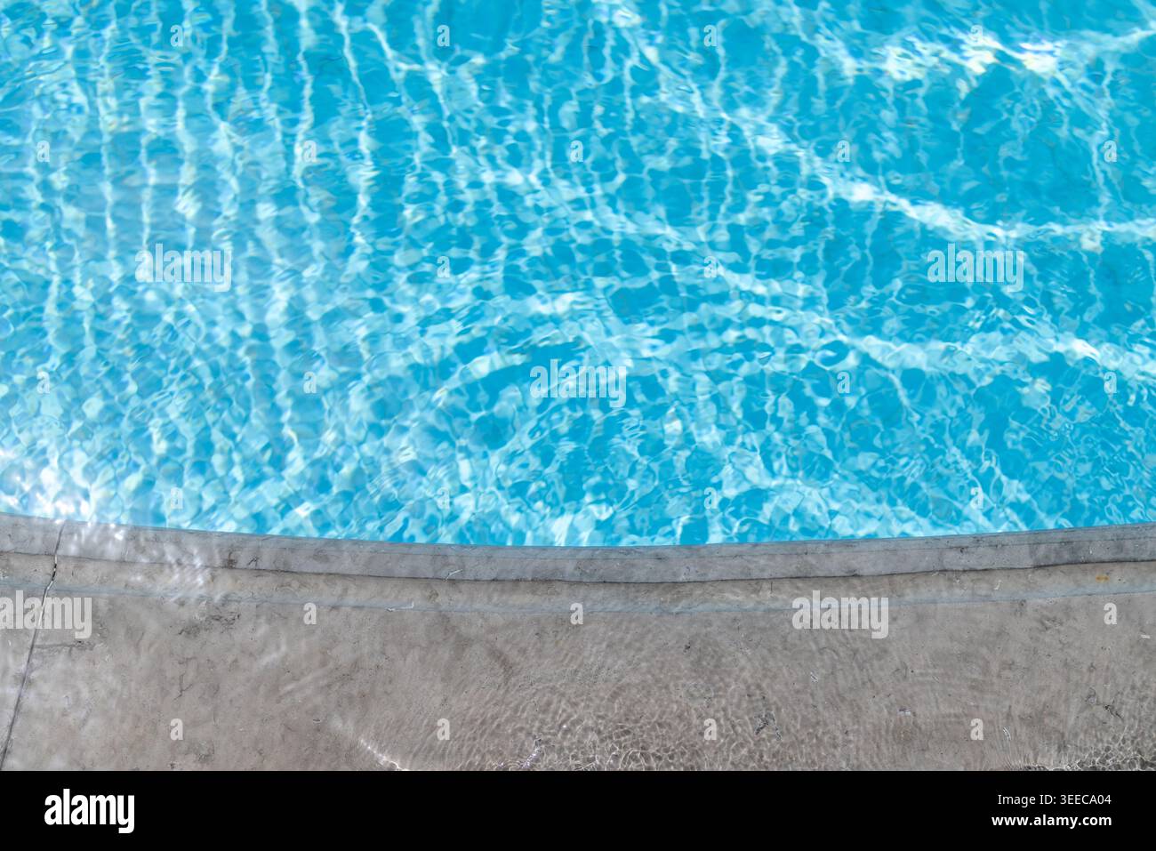 Bord de piscine en pierre incurvé à côté de l'eau turquoise éclatante avec des reflets scintillants créant un arrière-plan minimaliste calme pour le SUMM Banque D'Images