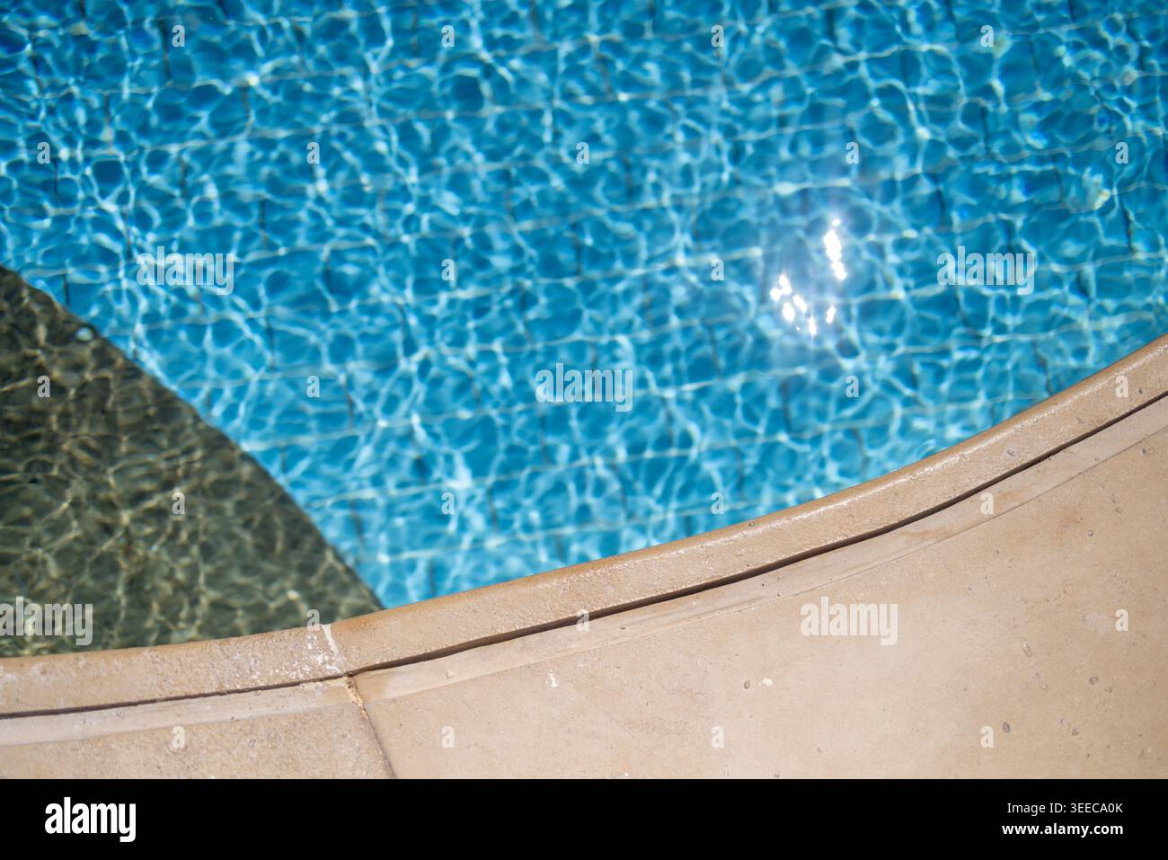 Bord de piscine beige incurvé à côté de l'eau turquoise éclatante avec des reflets scintillants créant un arrière-plan minimaliste calme pour le SUMM Banque D'Images