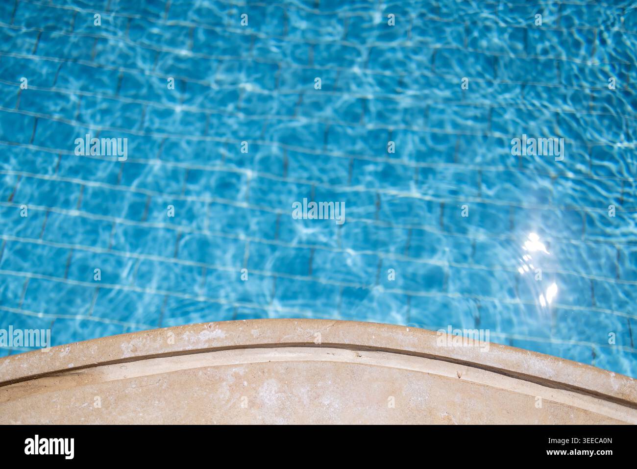 Bord de piscine beige incurvé à côté de l'eau turquoise éclatante avec des reflets scintillants créant un arrière-plan minimaliste calme pour le SUMM Banque D'Images