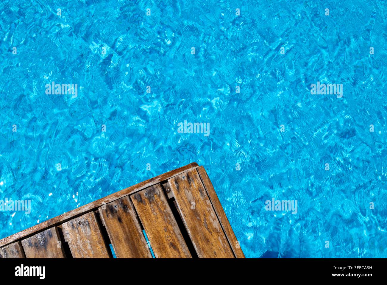Terrasse en bois à côté de l'eau turquoise lumineuse de la piscine avec des reflets chatoyants et des textures de surface ondulantes créant un calme de loisirs estivaux Banque D'Images