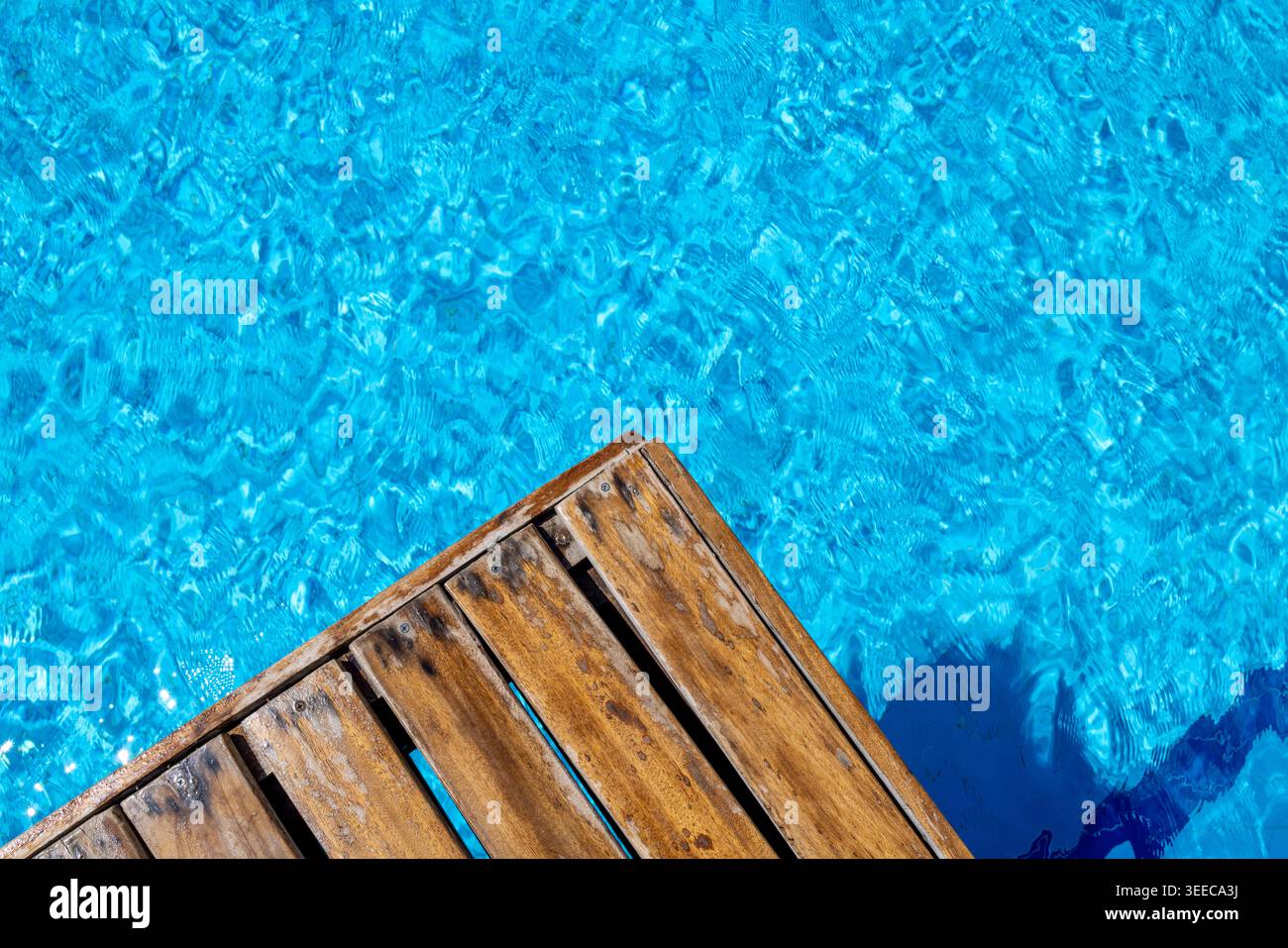 Terrasse en bois à côté de l'eau turquoise lumineuse de la piscine avec des reflets chatoyants et des textures de surface ondulantes créant un calme de loisirs estivaux Banque D'Images