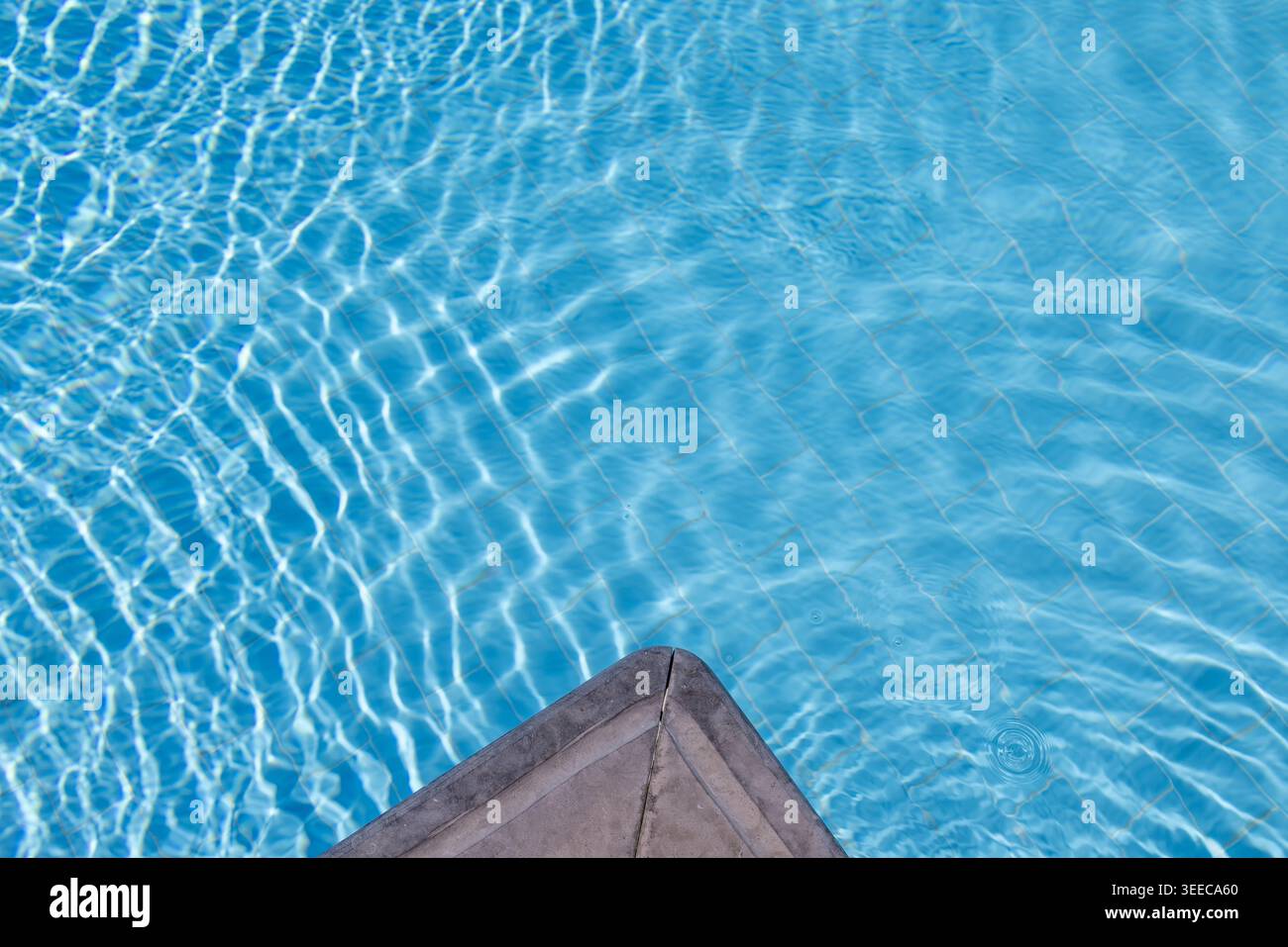 Coin de piscine en pierre minimal au-dessus de l'eau turquoise claire de la piscine avec des reflets scintillants créant un arrière-plan de villégiature de luxe calme pour su Banque D'Images