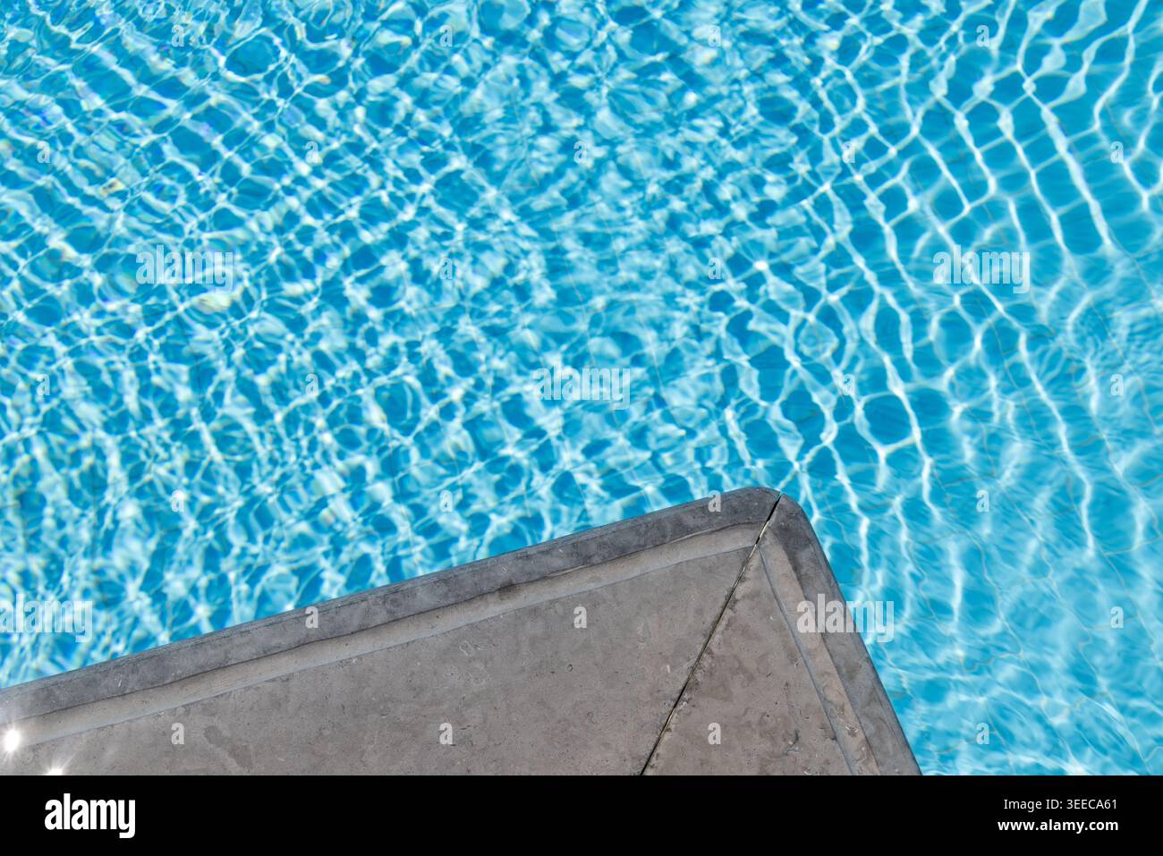 Coin de piscine en pierre minimal au-dessus de l'eau turquoise claire de la piscine avec des reflets scintillants créant un arrière-plan de villégiature de luxe calme pour su Banque D'Images