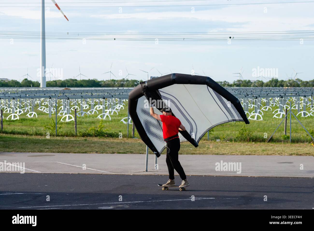 Skateboarder se préparant à utiliser une aile portative pour la propulsion éolienne sur une autoroute vide à proximité d'un parc éolien Banque D'Images