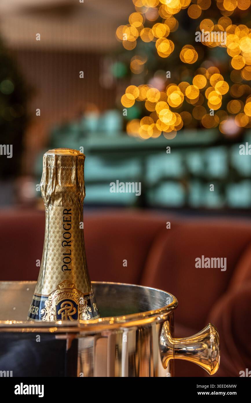 Une bouteille de champagne Pol Roger fraîche dans un seau à glace argenté, sur un fond chaleureux et festif avec des lumières de sapin de Noël éclatantes. Banque D'Images