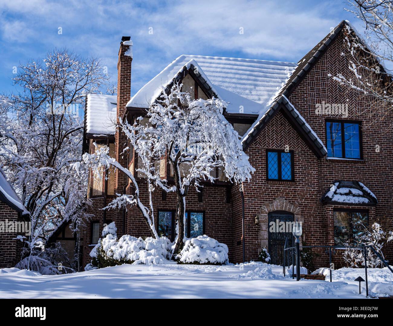 Une maison de style Tudor Revival avec un toit incliné à pignons, des colombages et une grande cheminée sur une belle journée d'hiver couverte de neige fraîchement tombée. Banque D'Images