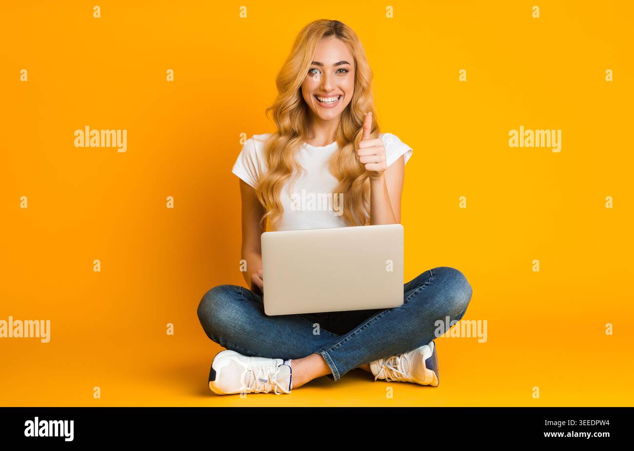 Femme joyeuse utilisant un ordinateur portable et montrant le pouce vers le haut Banque D'Images