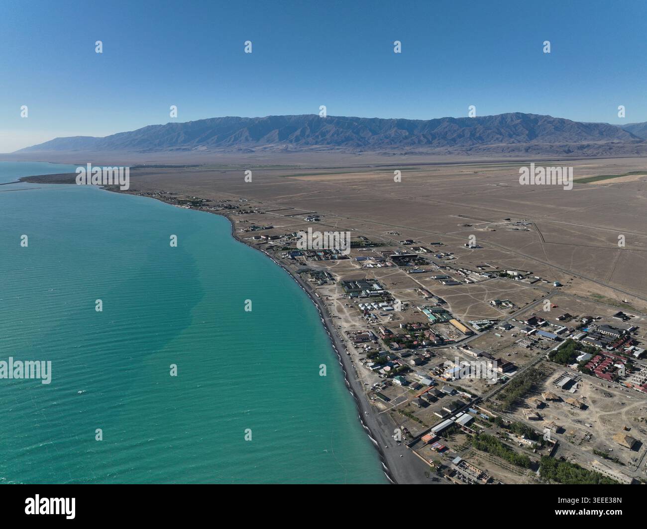 Une perspective aérienne capture une ville côtière située le long d'une mer turquoise vibrante, bordée par des plaines arides et des chaînes de montagnes lointaines sous clair Banque D'Images