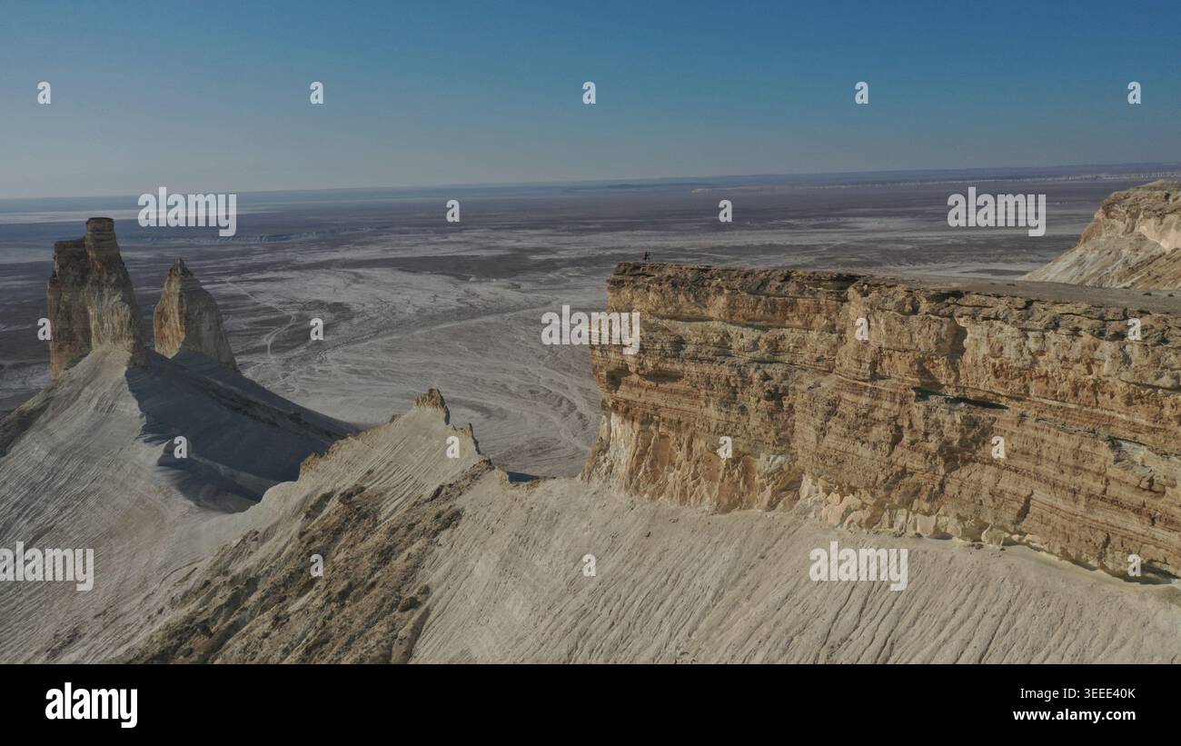 Une vue aérienne panoramique capture d'imposantes formations rocheuses s'élevant de façon spectaculaire d'un vaste paysage désertique aride sous un ciel bleu clair avec lisse Banque D'Images