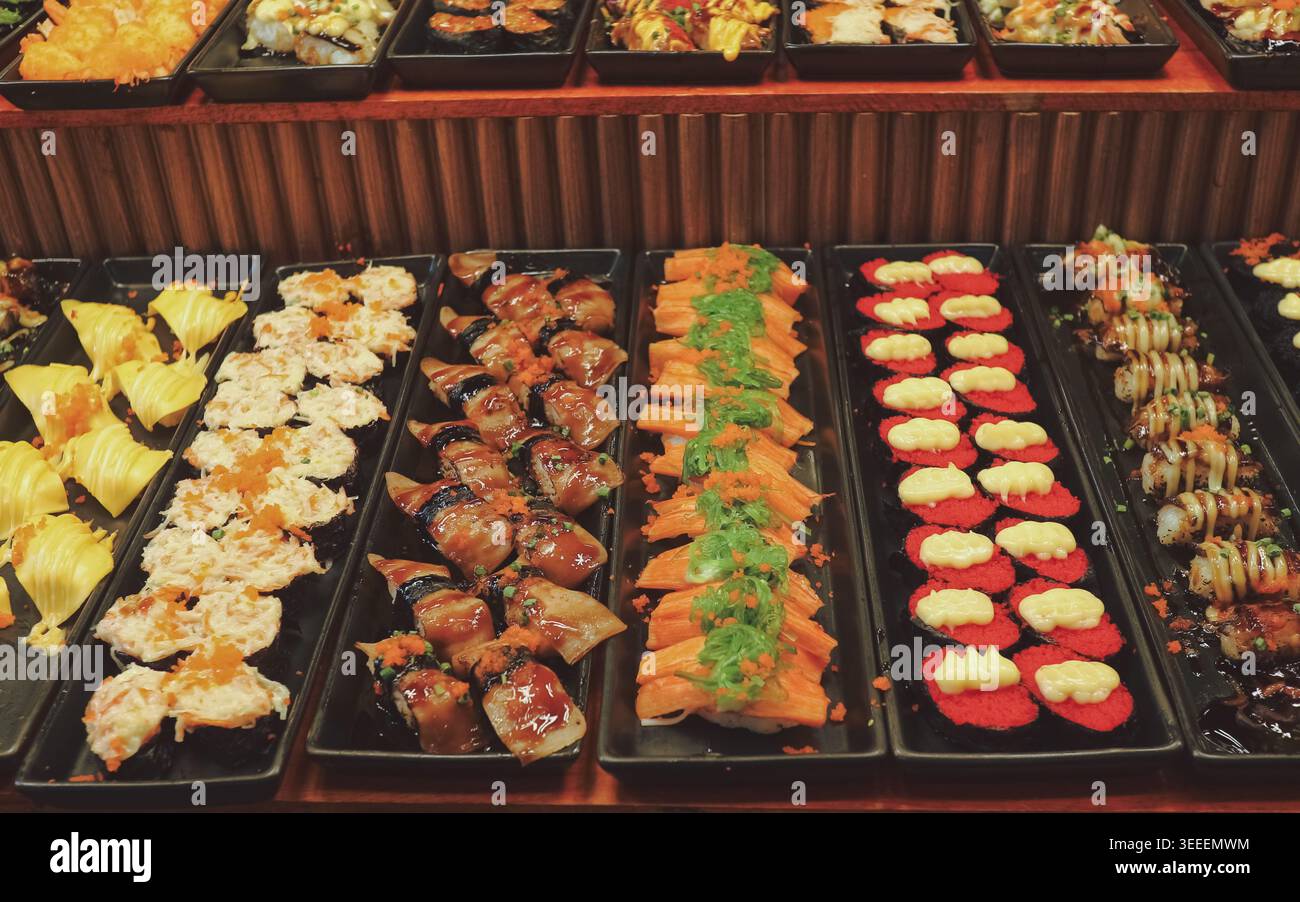 Vue sur la variété de rouleaux de sushi sur les plateaux du marché. Éclairage lumineux représentant la culture de la cuisine fusion japonaise authentique et les petites entreprises asiatiques. Banque D'Images