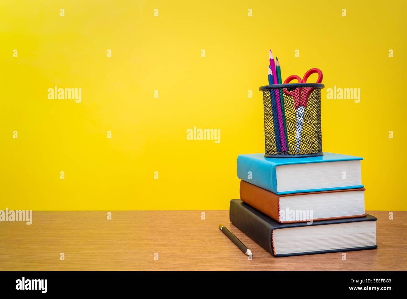 Une pile de trois livres et porte-crayon sur un fond jaune avec espace de copie. Banque D'Images
