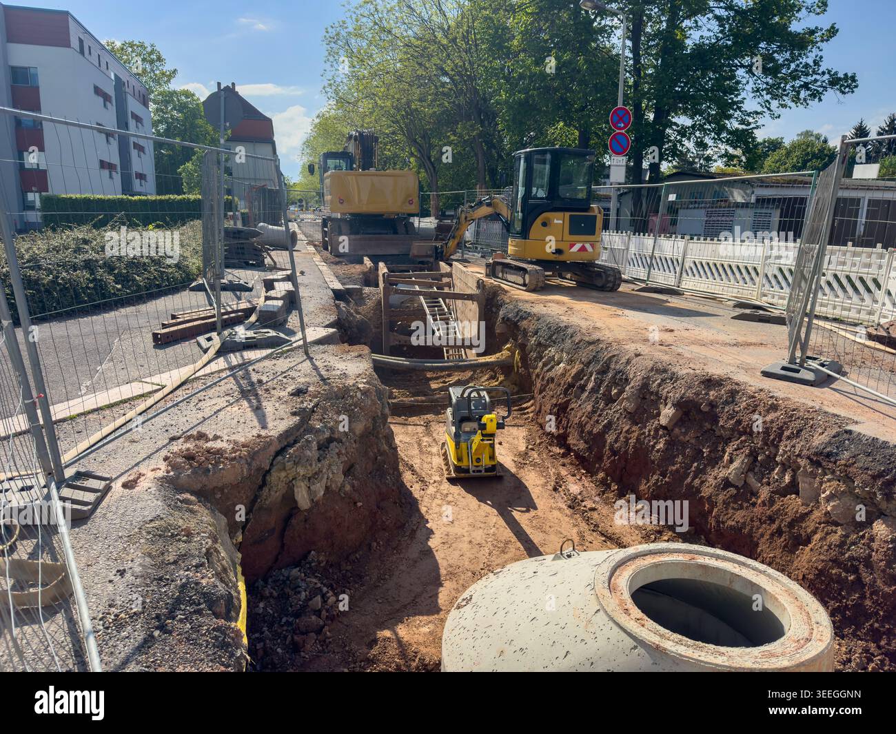 Chantier majeur de la ville : installation de conduites d'eau à l'aide d'une pelle et d'une plaque vibrante. Banque D'Images