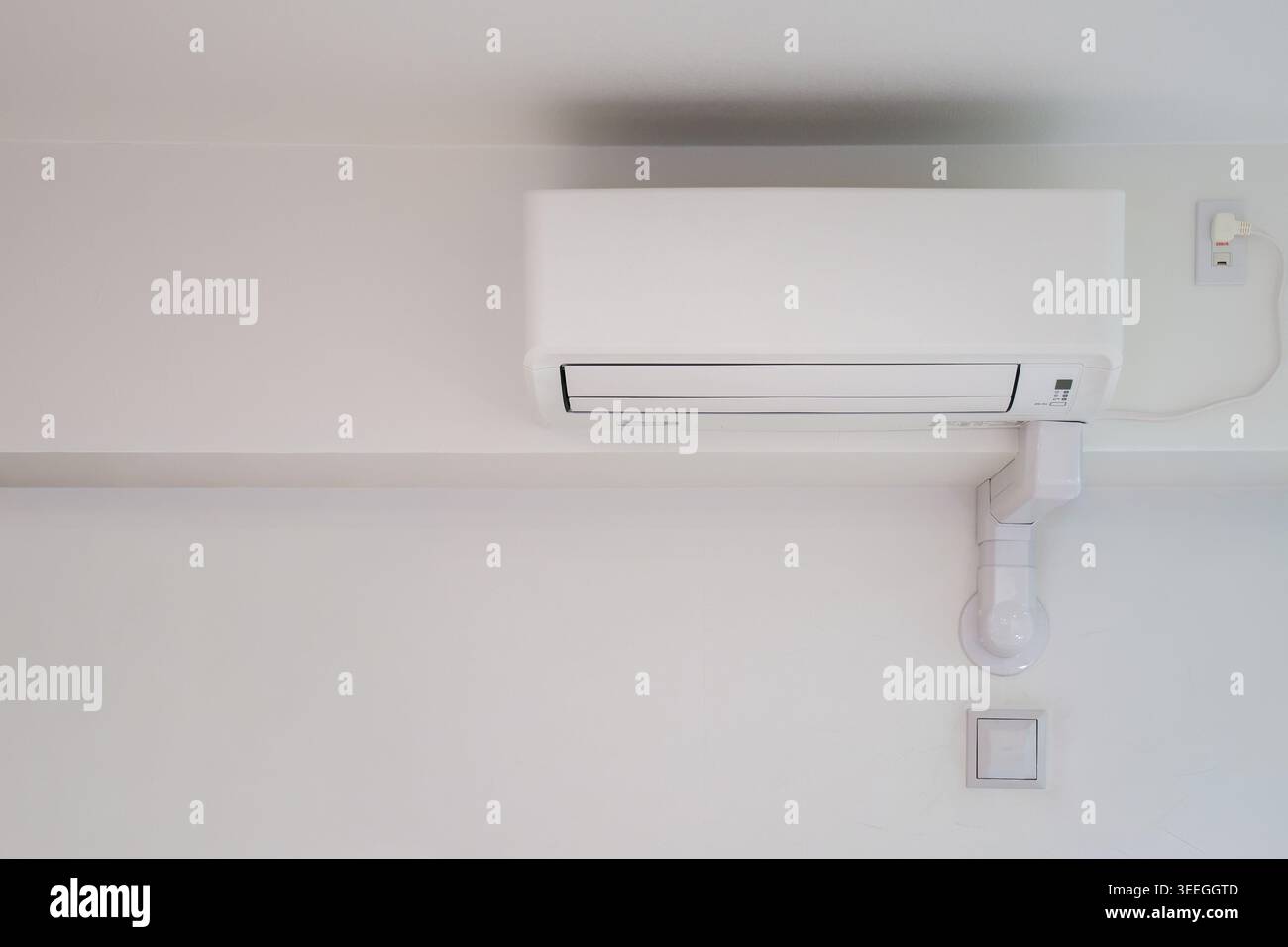 Unité de climatisation murale blanche installée sur un mur intérieur blanc propre avec tuyauterie blanche. Composition minimale idéale pour l'immobilier, la maison et le contenu intérieur. Banque D'Images