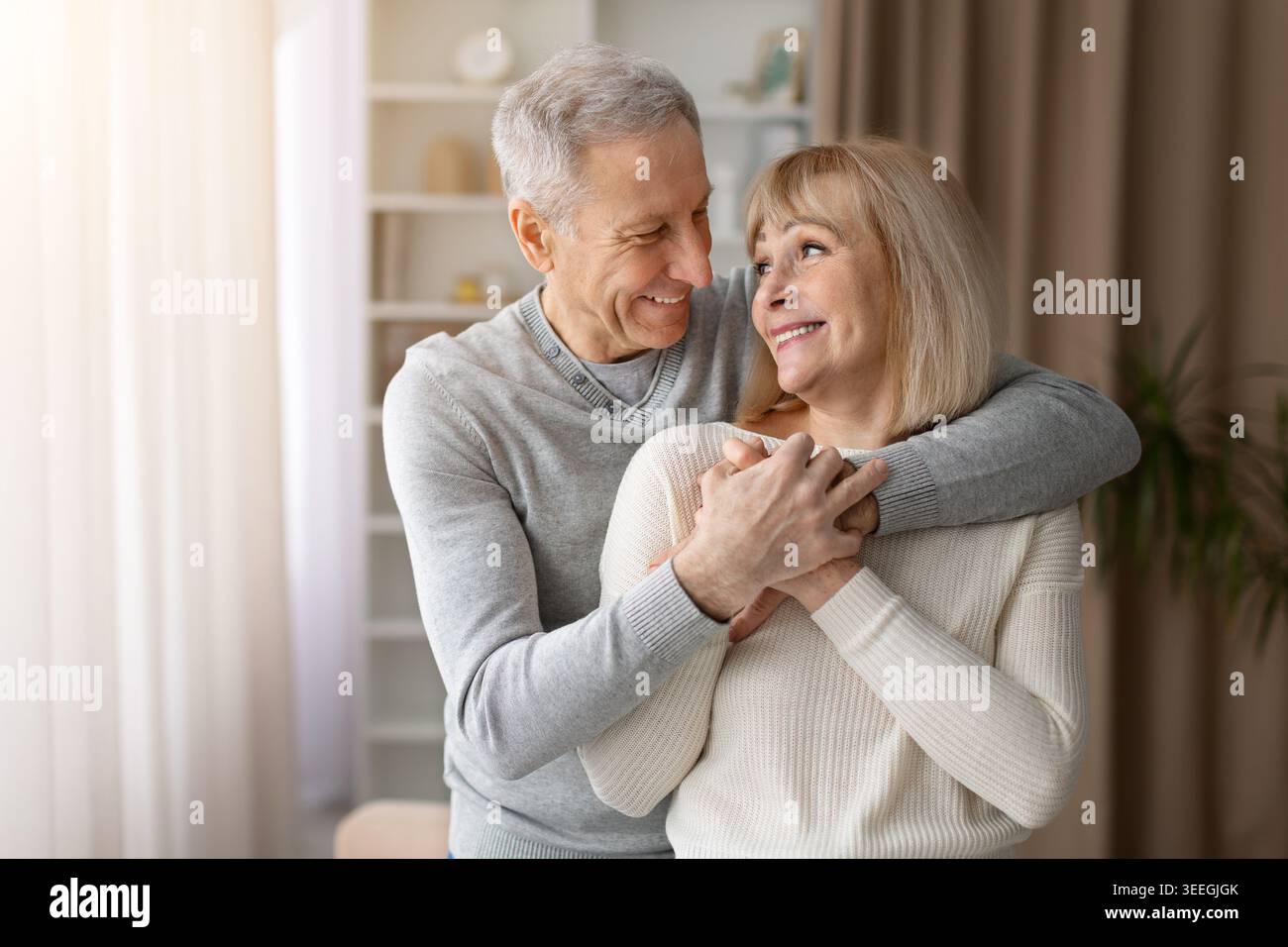 Heureux couple mature embrassant et souriant l'un à l'autre à la maison Banque D'Images