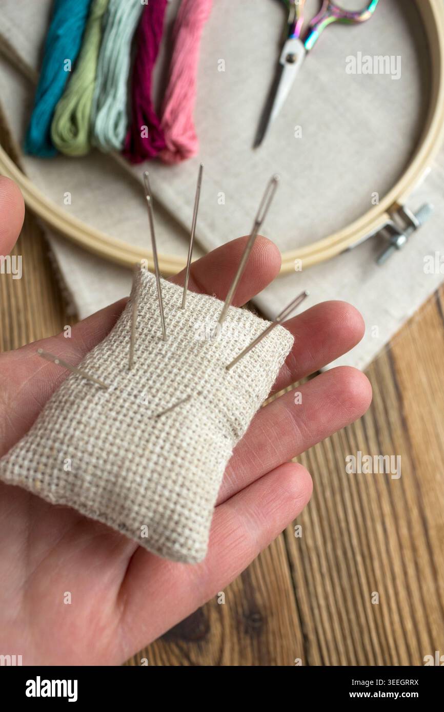 Outils et matériaux de broderie sur fond de bois : cerceau de broderie avec tissu de lin, fils colorés, coussin d'aiguille et ciseaux décoratifs. Besoin Banque D'Images