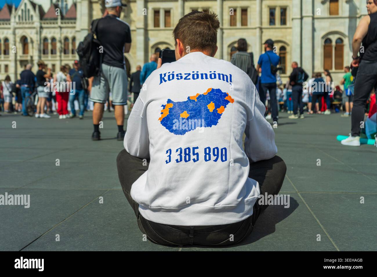 Un partisan du Parti Tisza portant la carte électorale hongroise de 2026 regarde la session inaugurale du parlement sur la place Kossuth à Budapest. Banque D'Images