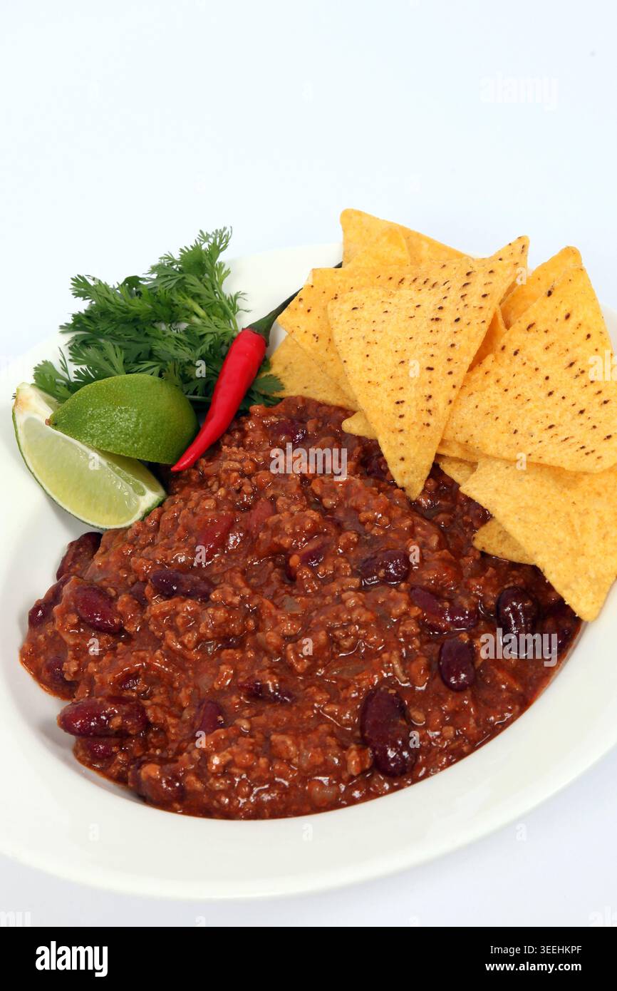 Un Chilli Con Carne servi avec du citron vert, de la coriandre, un piment rouge et des chips de tortilla. Banque D'Images