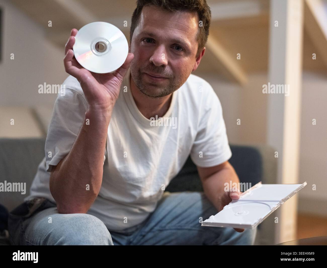 Homme regardant un disque compact assis dans un salon Banque D'Images