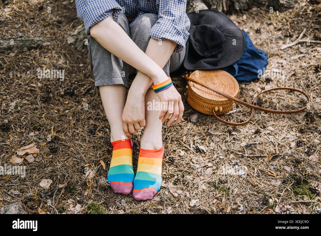 La personne est assise sur le sol de la forêt portant des chaussettes arc-en-ciel et un bracelet. Expression de l'identité de genre, représentation LGBTQ dans les médias, vie queer authentique. Banque D'Images