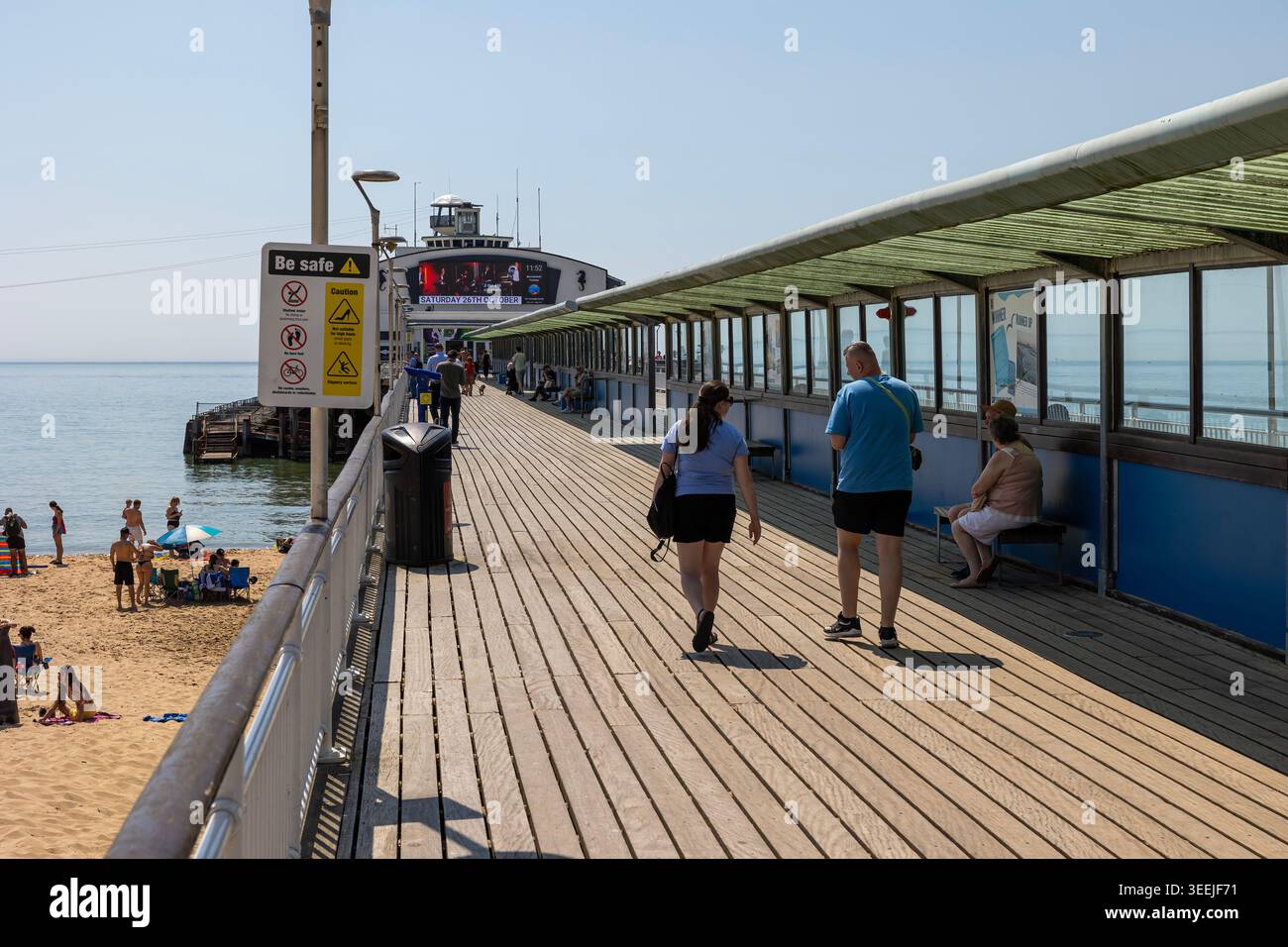 Les gens marchant sur la jetée de Bournemouth, Dorset, Angleterre - balade détendue en bord de mer sous un ciel bleu clair. Banque D'Images