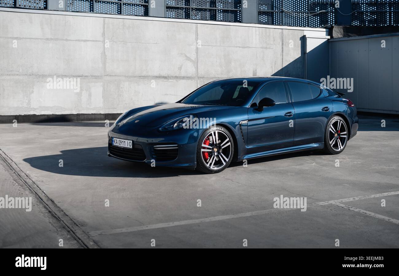 Porsche Panamera bleue devant un mur de béton le jour ensoleillé. Vue de trois quarts de face du grand randonneur allemand dans le parking sur le toit. Banque D'Images