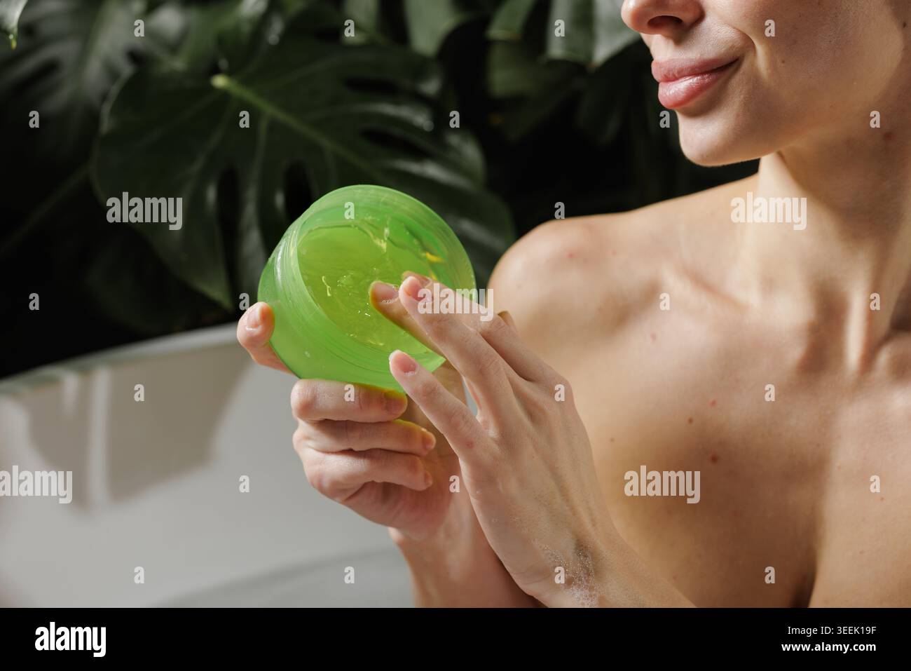 Une femme applique doucement le gel d'aloe vera sur sa peau, entourée d'une végétation luxuriante, mettant en valeur une routine de soins naturels parfaite pour la beauté et le bien-être Banque D'Images